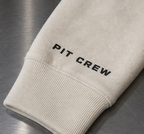 Ivory hoodie with ONE front artwork, PIT CREW sleeve lettering, and an 01 neck label. — Sleeve application