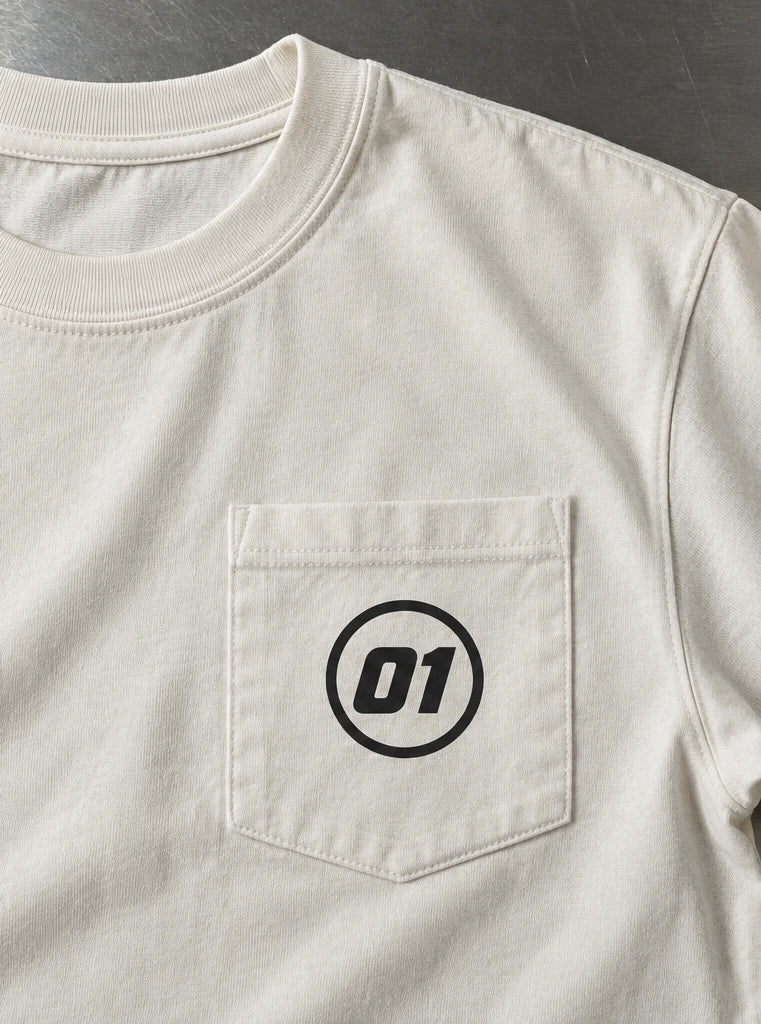Charcoal youth T-shirt with a compact ONE front graphic beside an ivory shirt pocket with a small 01 logo inside the seams. — Pocket application